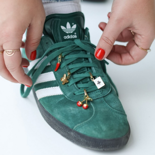 Green Adidas sneaker with decorative charms being adjusted by a person.