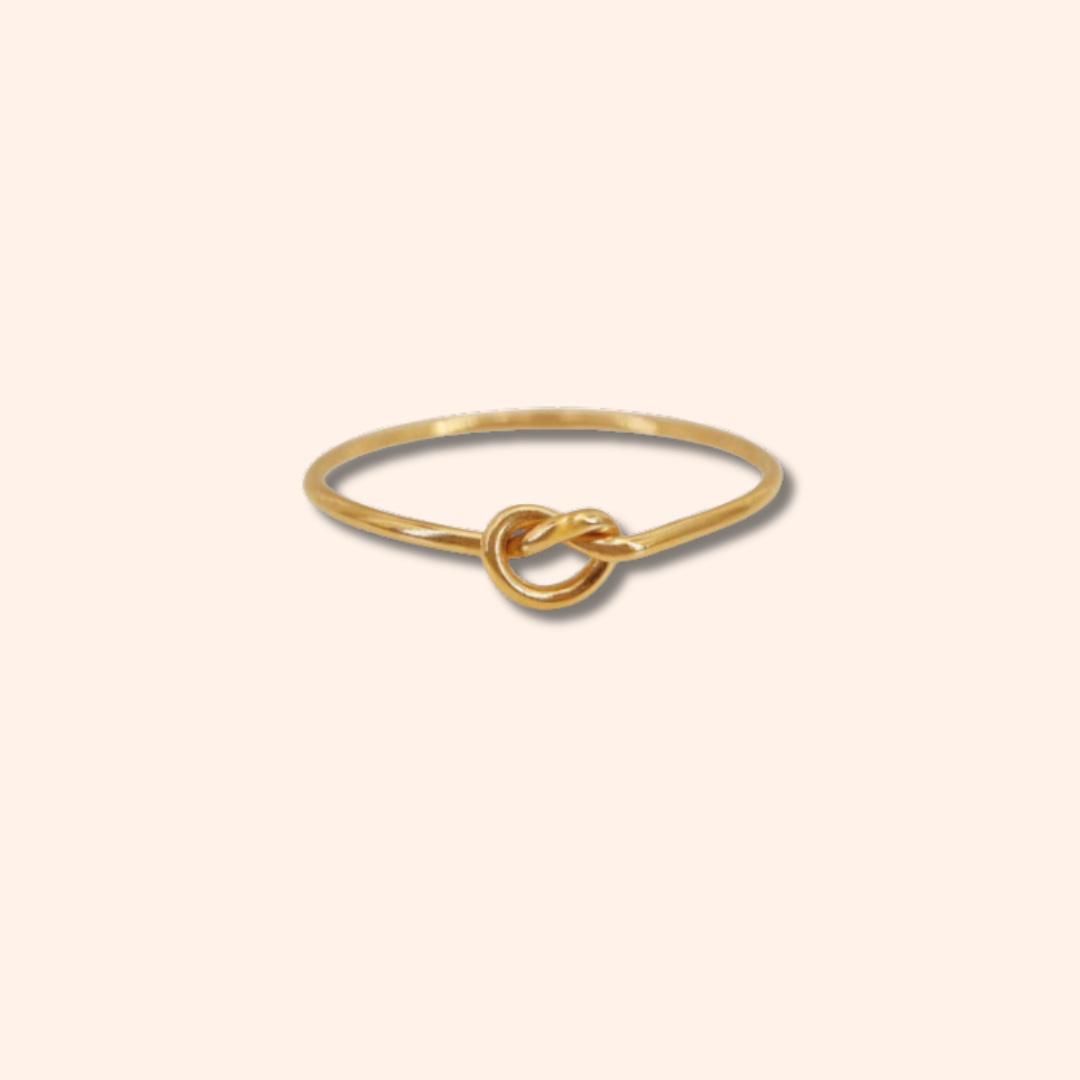 Gold ring with a knot design on a light beige background