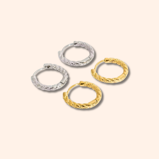 Four gold and silver hoop earrings on a light beige background