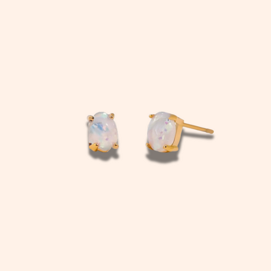 Pair of gold earrings with opal stones on a beige background
