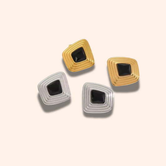 Pair of earrings with square design and black center on a beige background