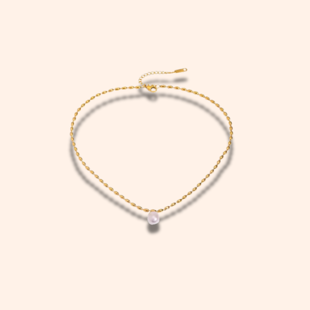 Gold necklace with a single pearl on a light beige background