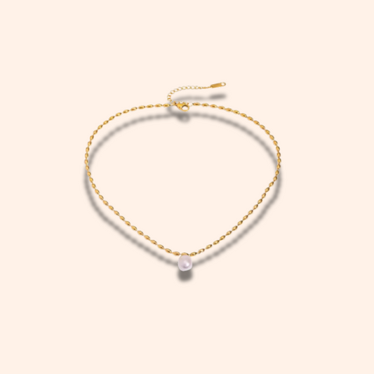 Gold necklace with a single pearl on a light beige background