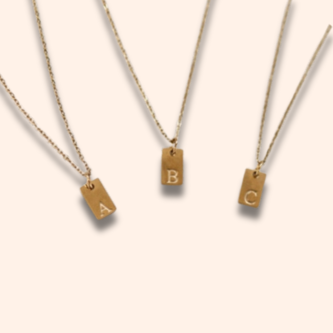 Three gold necklaces with letter pendants on a beige background