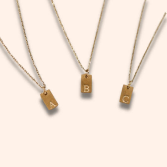 Three gold necklaces with letter pendants on a beige background