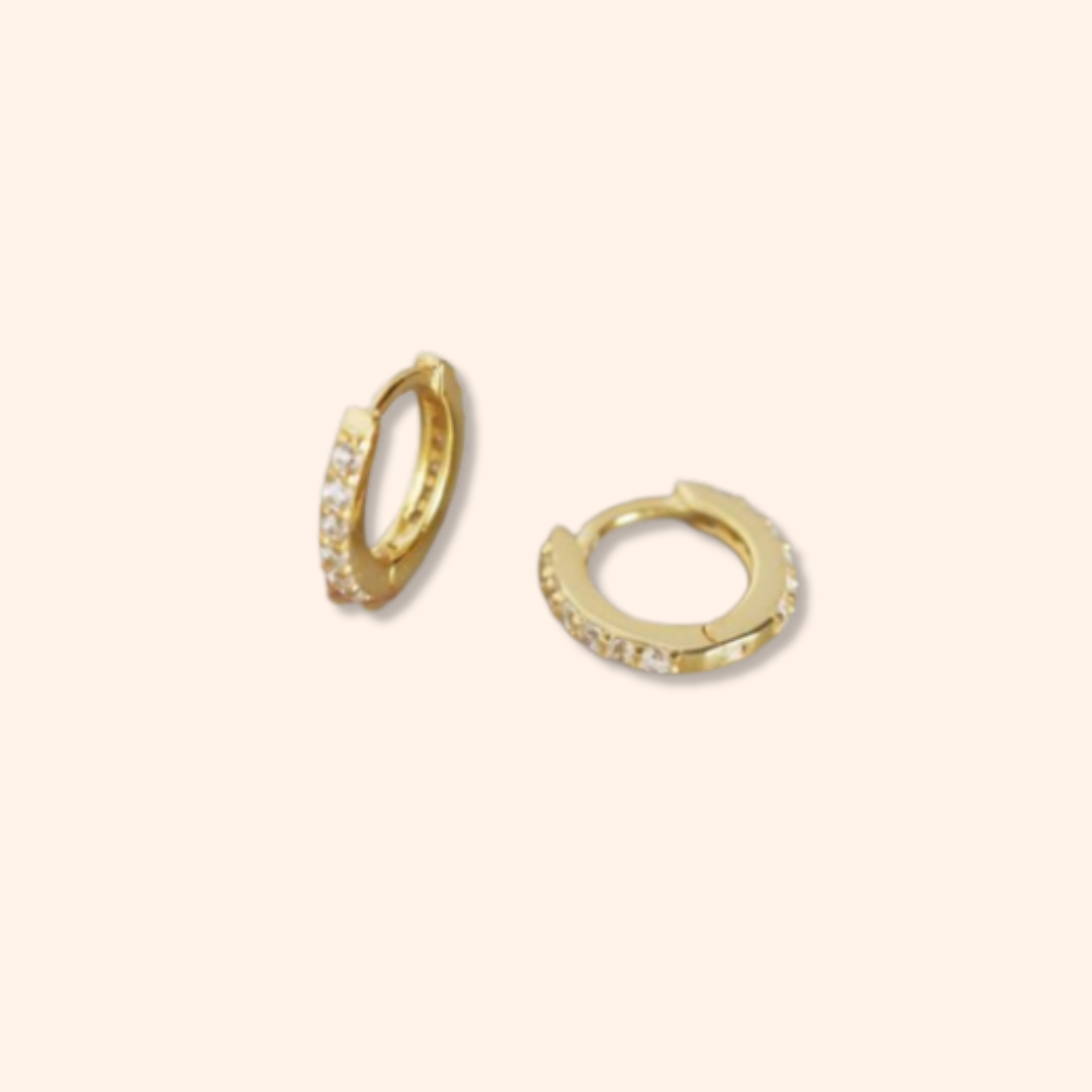 Gold hoop earrings with embedded stones on a beige background