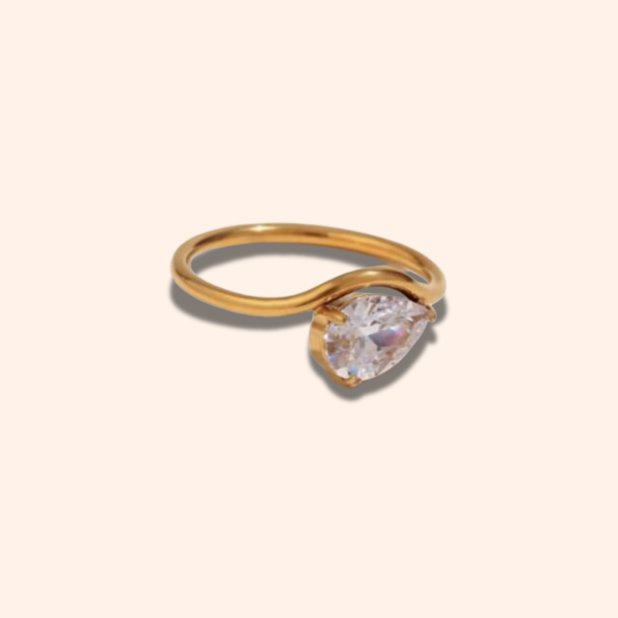 Gold ring with a pear-shaped diamond on a light beige background
