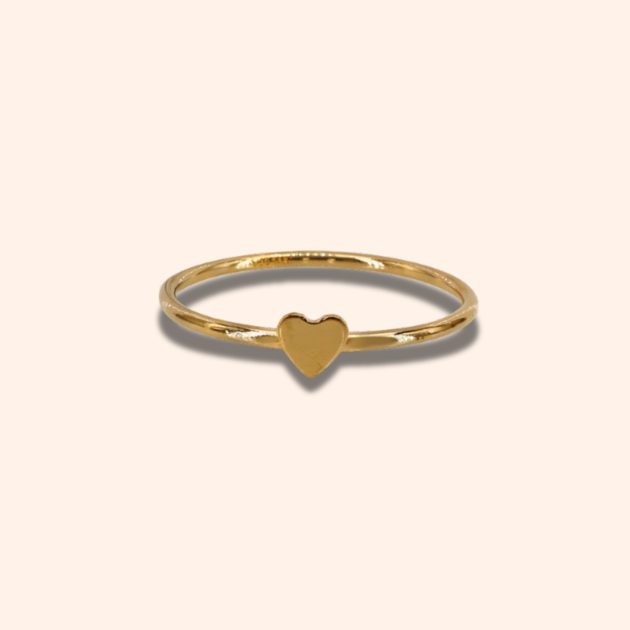 Gold ring with a heart-shaped charm on a beige background
