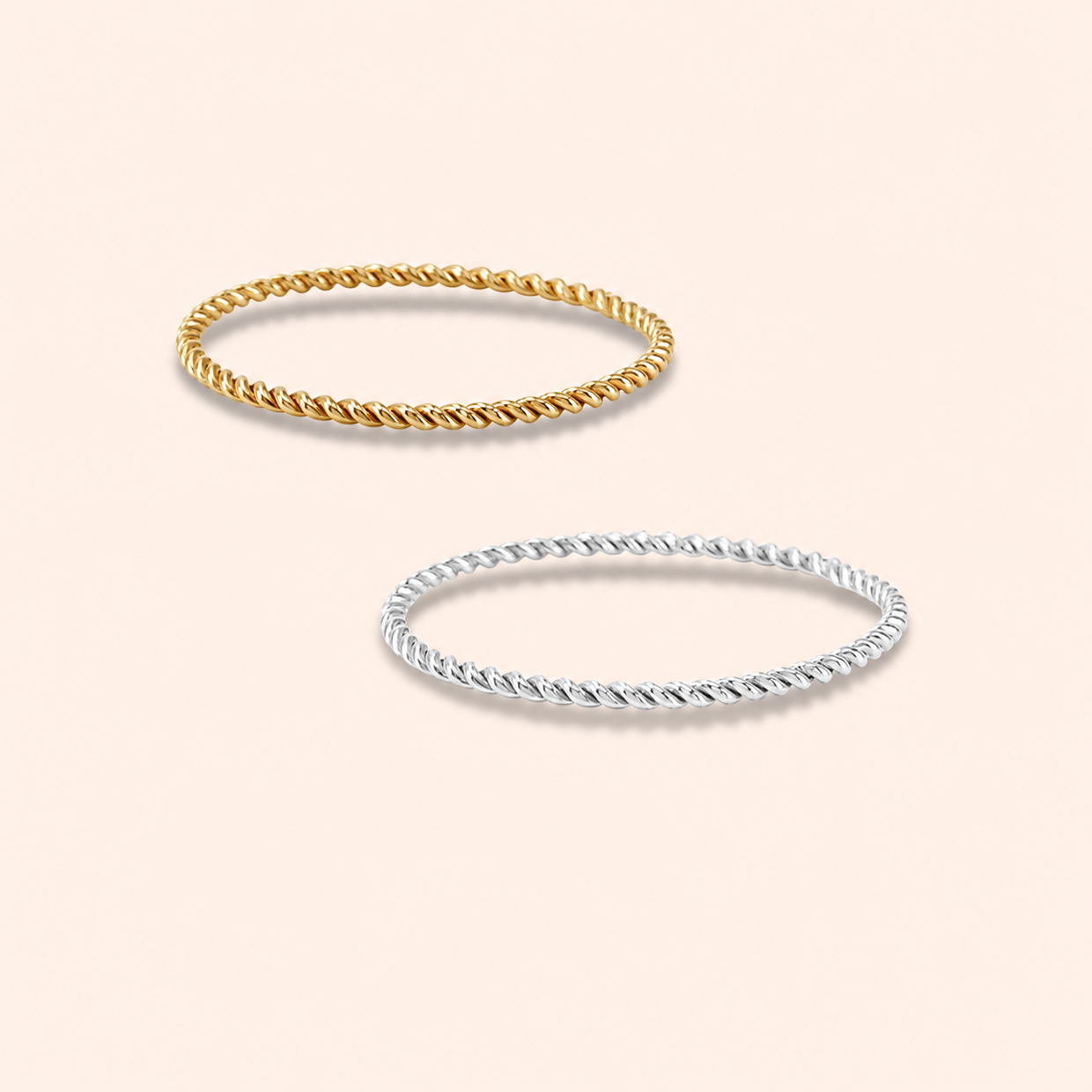 Two twisted rope-style bangles, one in yellow gold and one in silver, displayed on a light peach background.