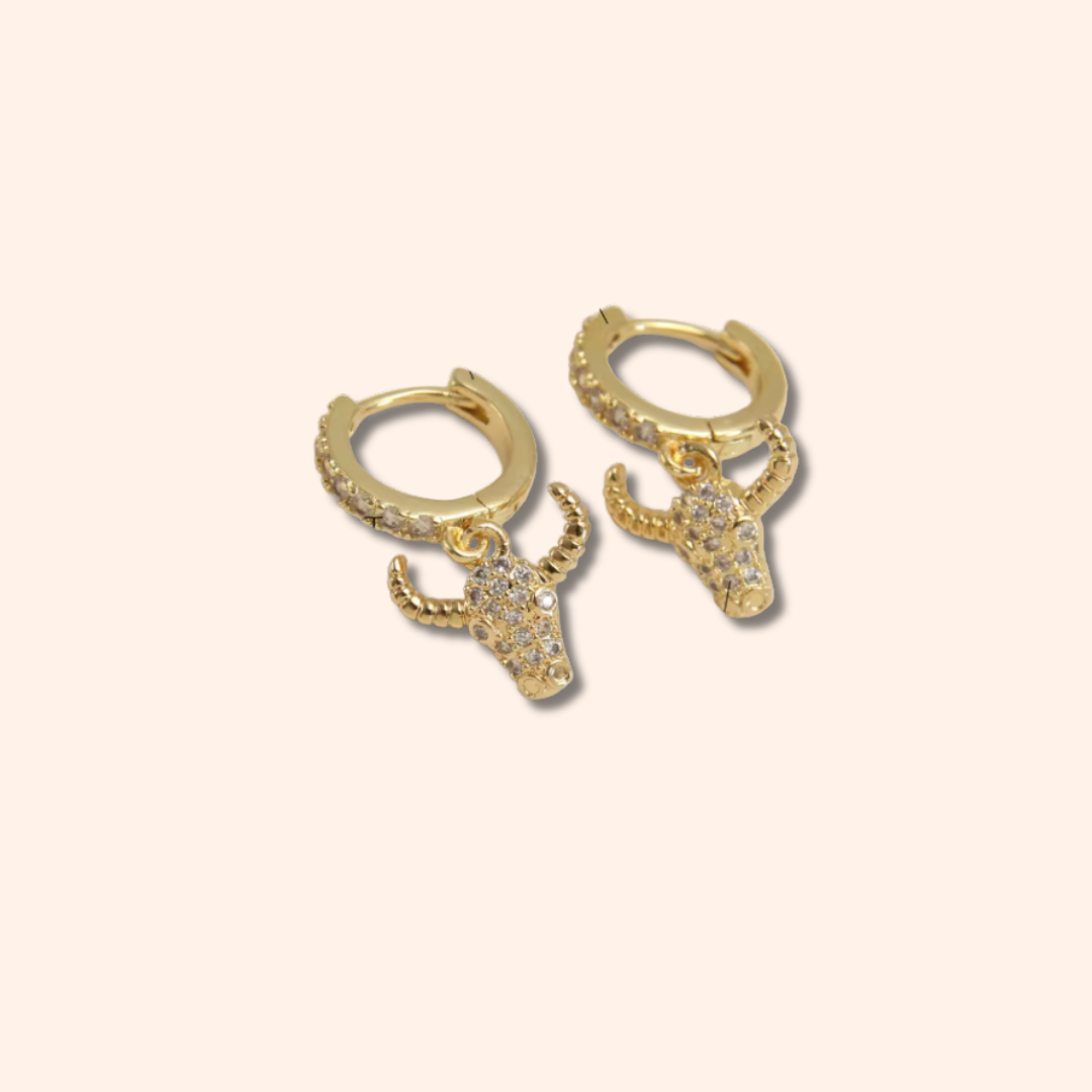 Gold bull head earrings on a beige background