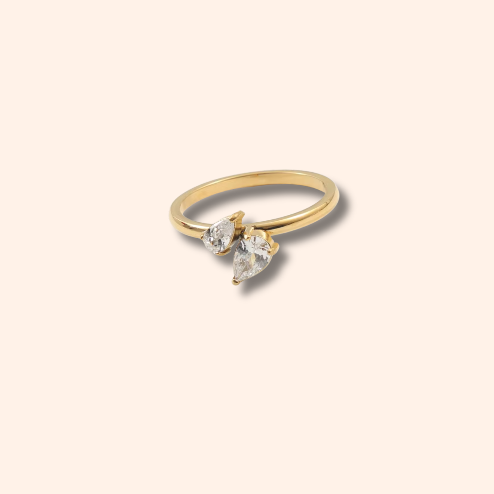 Gold ring with three clear gemstones on a beige background