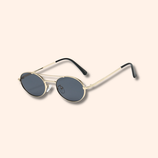 Oval sunglasses with a cream double-bridge metal frame, dark gray lenses, and black temple tips, shown on a solid pale beige background.