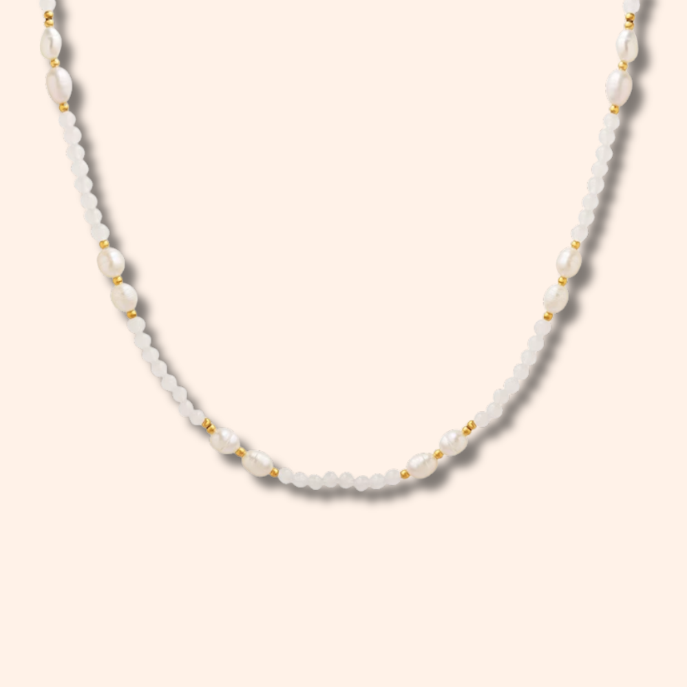 A delicate white beaded necklace with small gold spacer beads, displayed against a solid pale peach background.