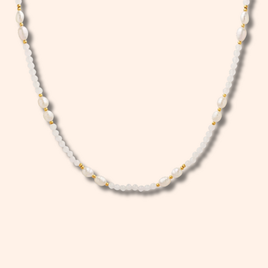 A delicate white beaded necklace with small gold spacer beads, displayed against a solid pale peach background.