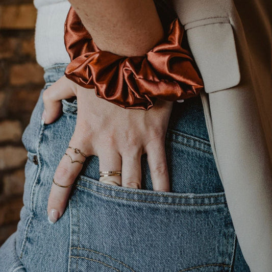 Person wearing a rust-colored scrunchie on wrist with denim jeans and neutral jacket.